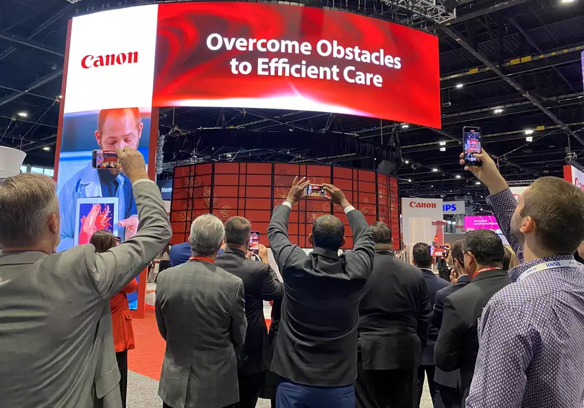 Attendees video record the curtain rising to unveil two new AI-enhanced Canon CT scanners at RSNA 2023. The vendor said both scanners will be aimed at the growing cardiac CT market. Photo by Dave Fornell
