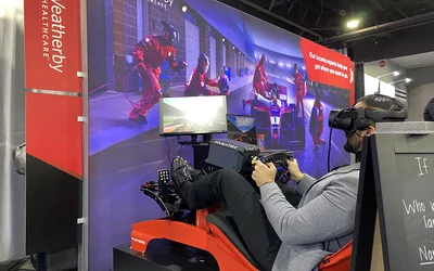 Attendee driving a race car simulator in a booth on the ACC.24 expo floor.